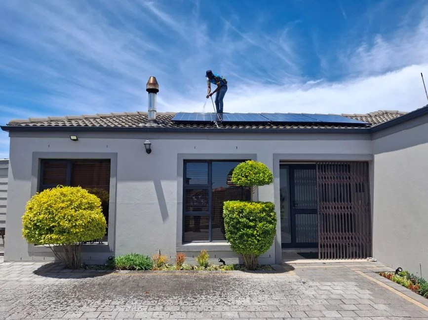 A male window cleaner washing the exterior glass roof from above with a tool during daylight.